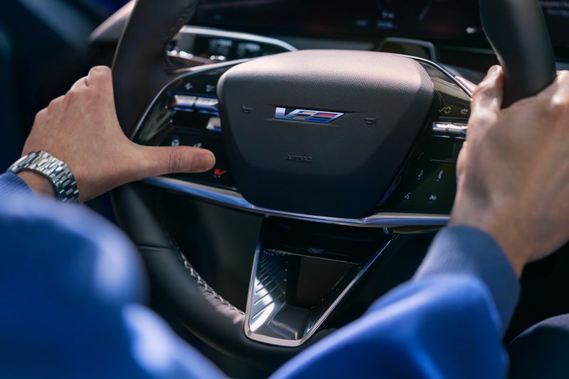 Close-up of a Man About to Press the V-Button on the 2026 OPTIQ-V Steering Wheel | Reliable Cadillac in Roseville CA